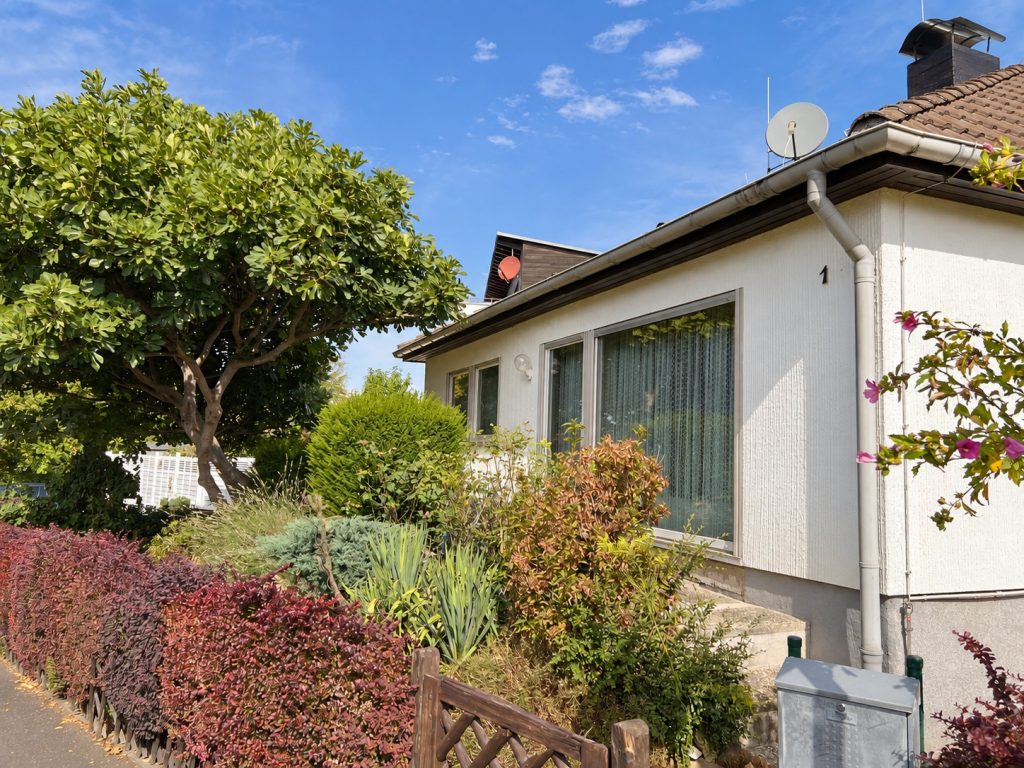 Gartenansicht des Bungalows mit großer Fensterfront, Bäumen und eingewachsenen Beeten