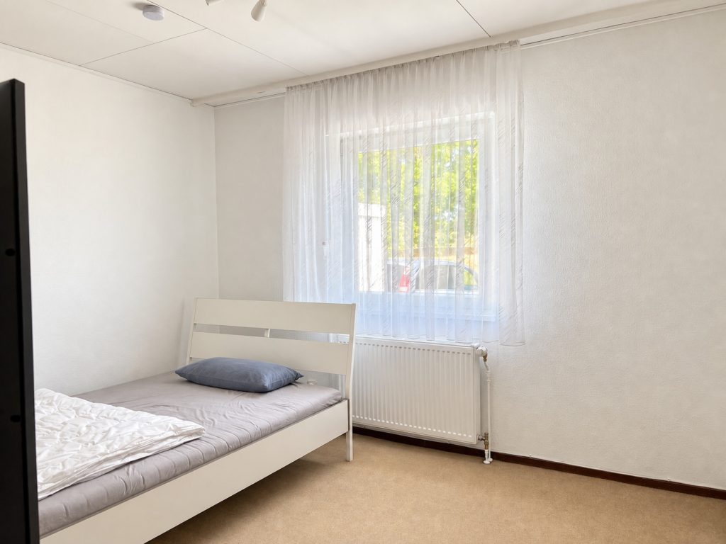 Schlafzimmer mit Einzelbett, großem Fenster und Blick in den Garten