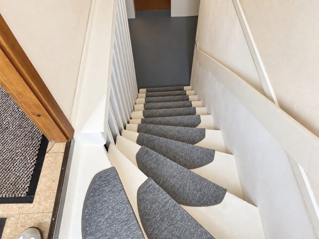 Treppe zum Kellergeschoss mit grauen Stufenmatten und weißem Handlauf